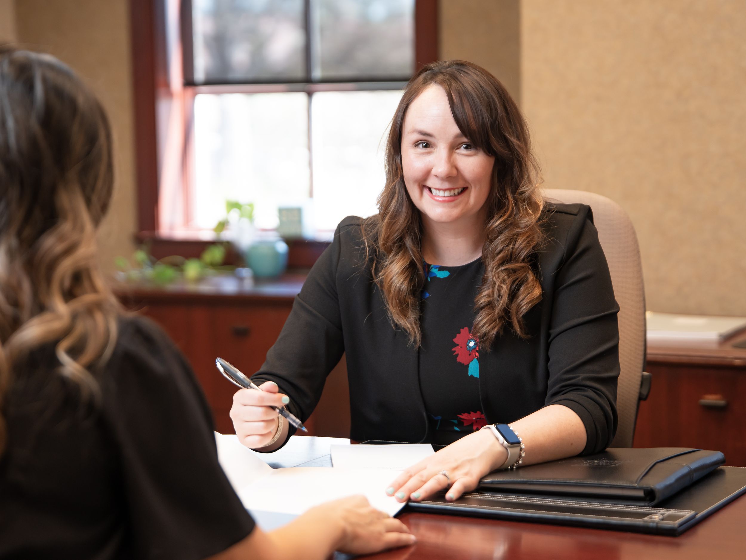 Professional meeting between two people at a desk in an office with natural light coming through the window.
