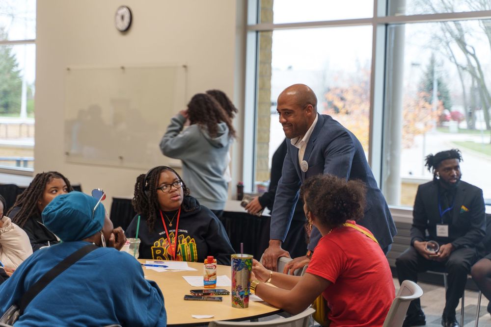 Students gather around a table in a cafeteria setting while engaged in discussion at an educational institution.