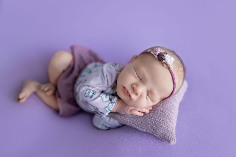 Sleeping baby in purple outfit resting on heart-shaped pillow.