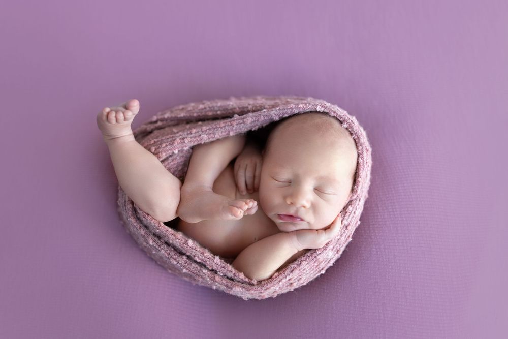 Newborn sleeping peacefully wrapped in purple knit blanket.