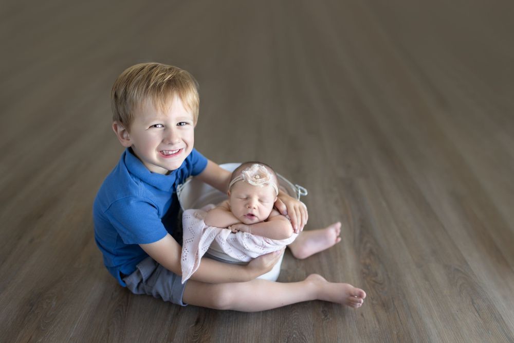 Two siblings seated on wooden floor sharing tender moment.