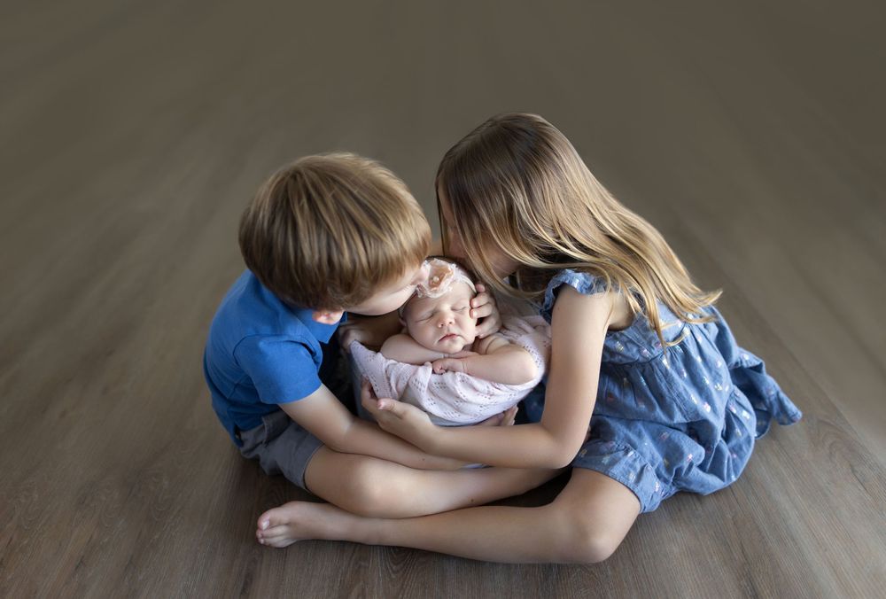 Three siblings sharing intimate moment on hardwood floor.