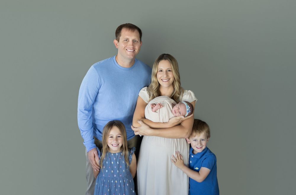 Family of four posing together against grey background in coordinated outfits.