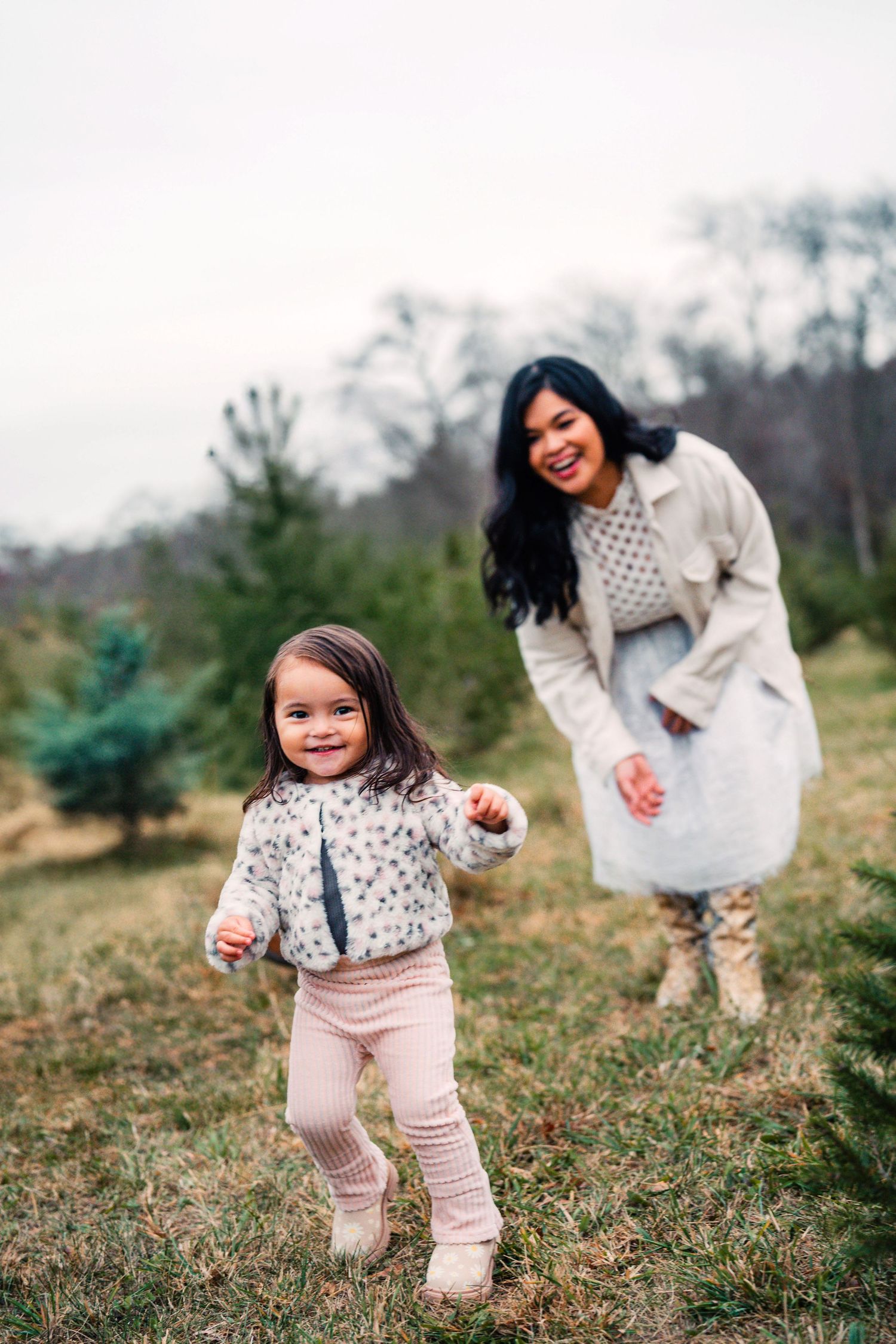 A parent and child wearing matching textured sweaters play together in a grassy field on an overcast day.