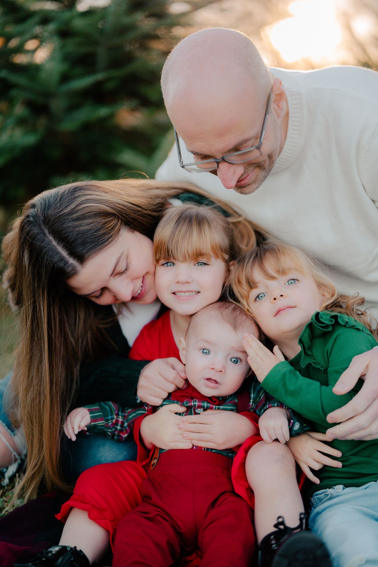 A sweet family portrait outdoors with seasonal red and green outfits against an evergreen background.