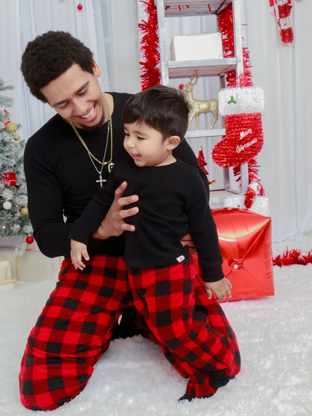 A heartwarming holiday moment with matching buffalo plaid pajama pants in front of Christmas decorations.