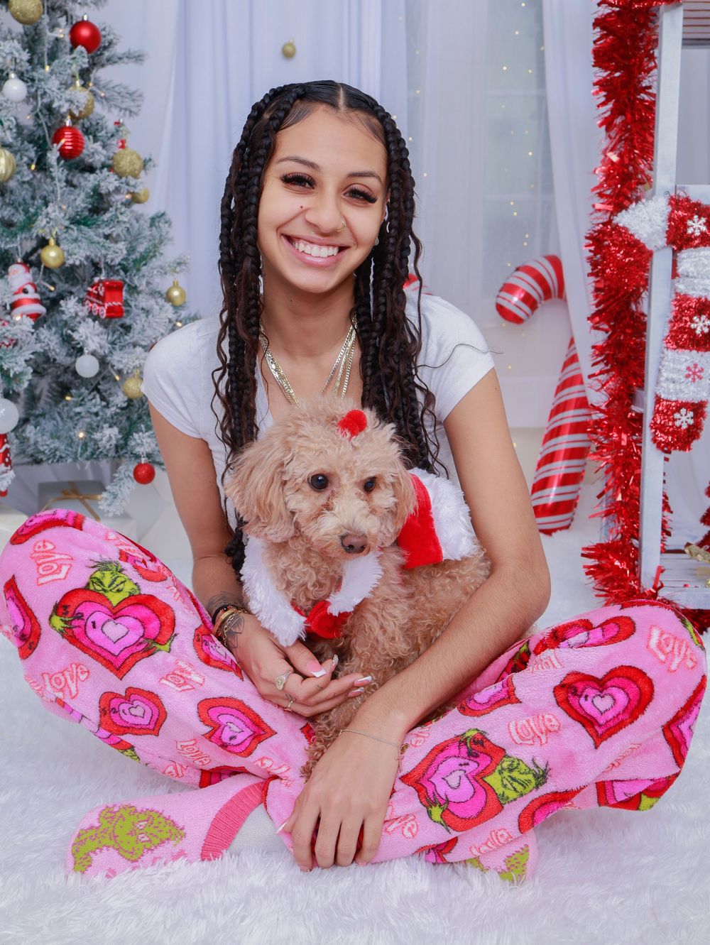 A festive holiday scene with someone wearing heart pajamas holding a small brown dog near a decorated Christmas tree.