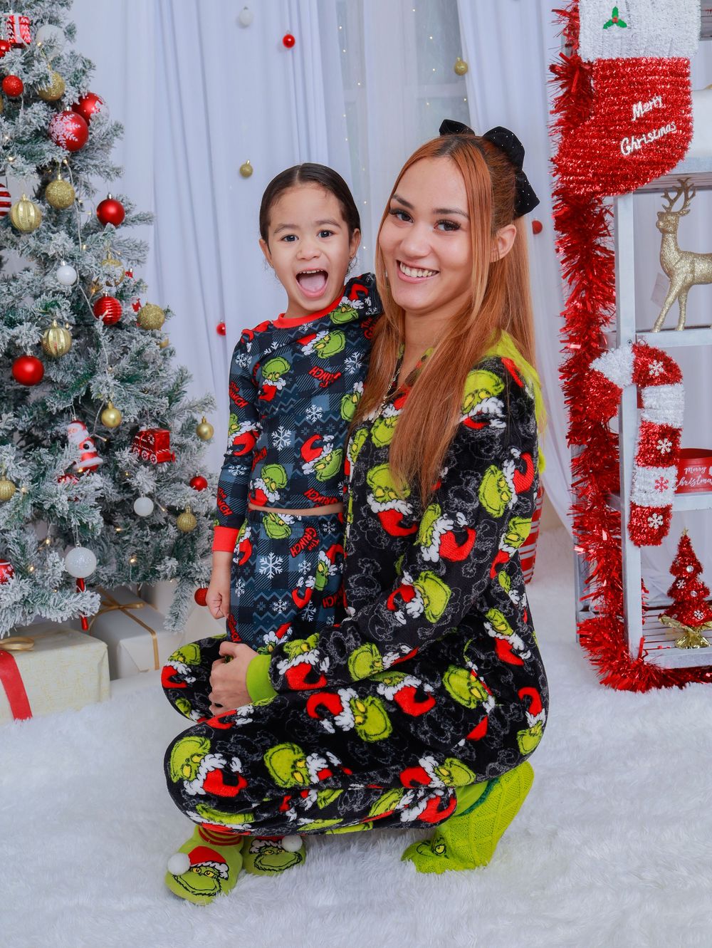 A fun holiday photo featuring matching Grinch pajamas and playful expressions near a Christmas tree.
