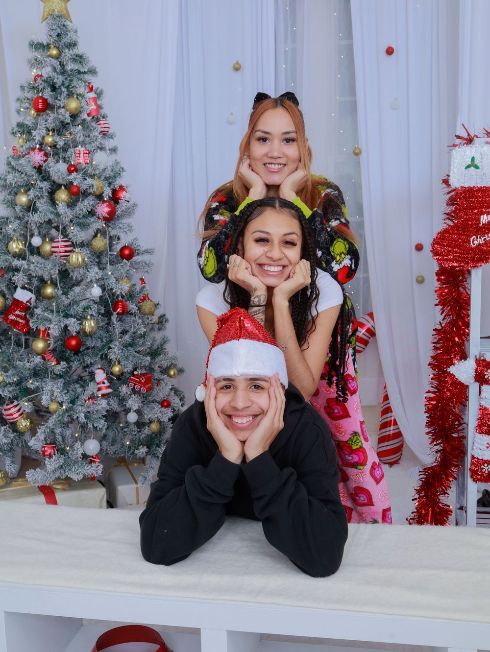 A creative stacked holiday portrait with three people posing in front of a Christmas tree.
