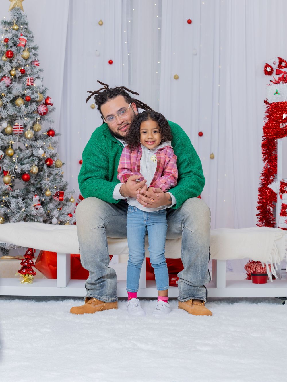 A festive holiday photoshoot with a decorated Christmas tree and red ornaments in the background.