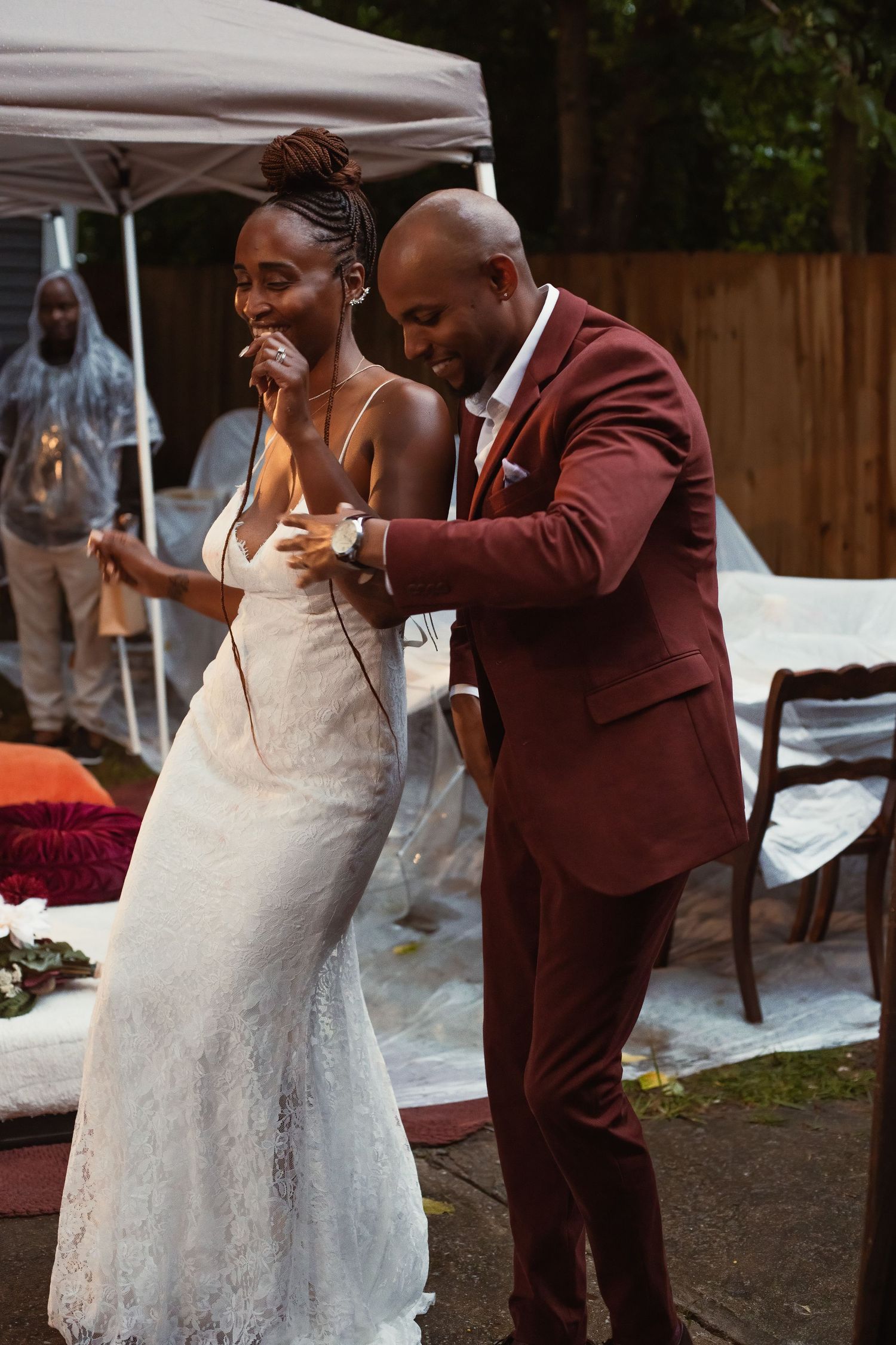 A couple poses together outdoors, with one wearing a tan suit and the other in a vibrant orange dress and green heels.