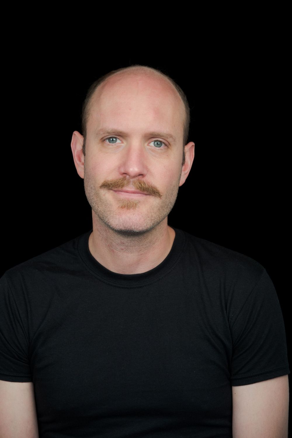 Close-up portrait of man with mustache wearing black t-shirt.