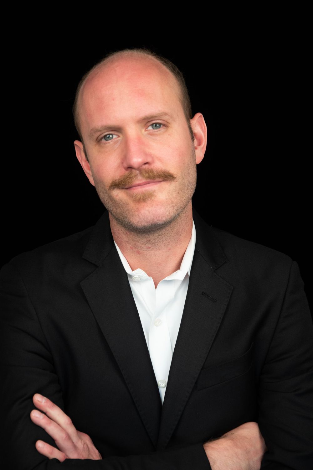 Professional headshot of man in suit jacket and white shirt against black background.