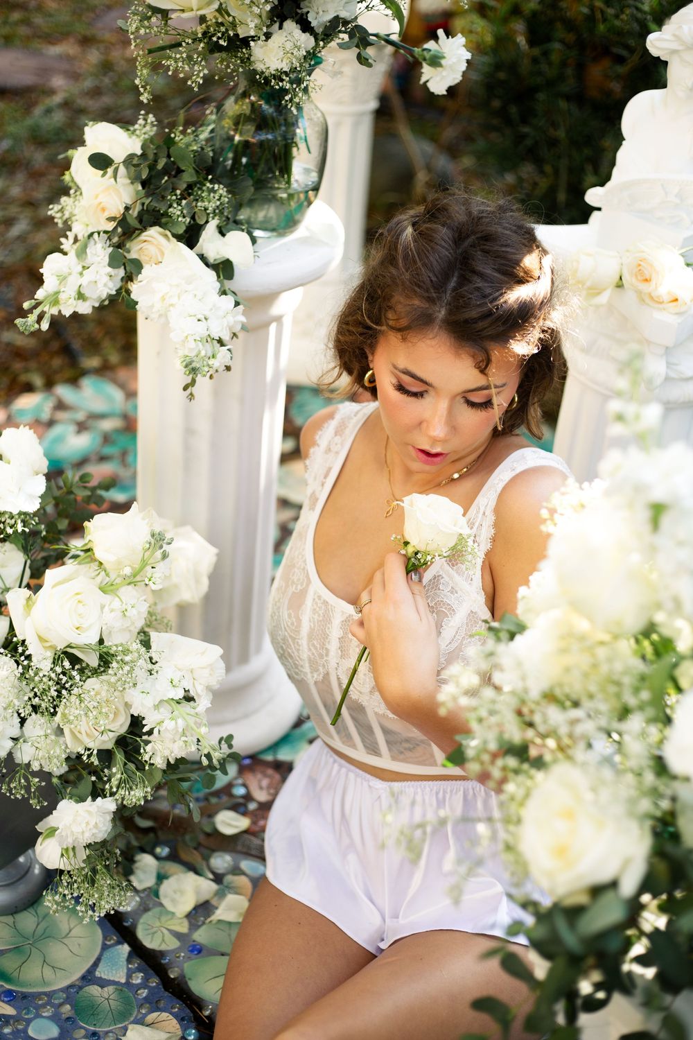 Romantic bridal boudoir photo with white flowers and lace lingerie in an elegant garden setting.