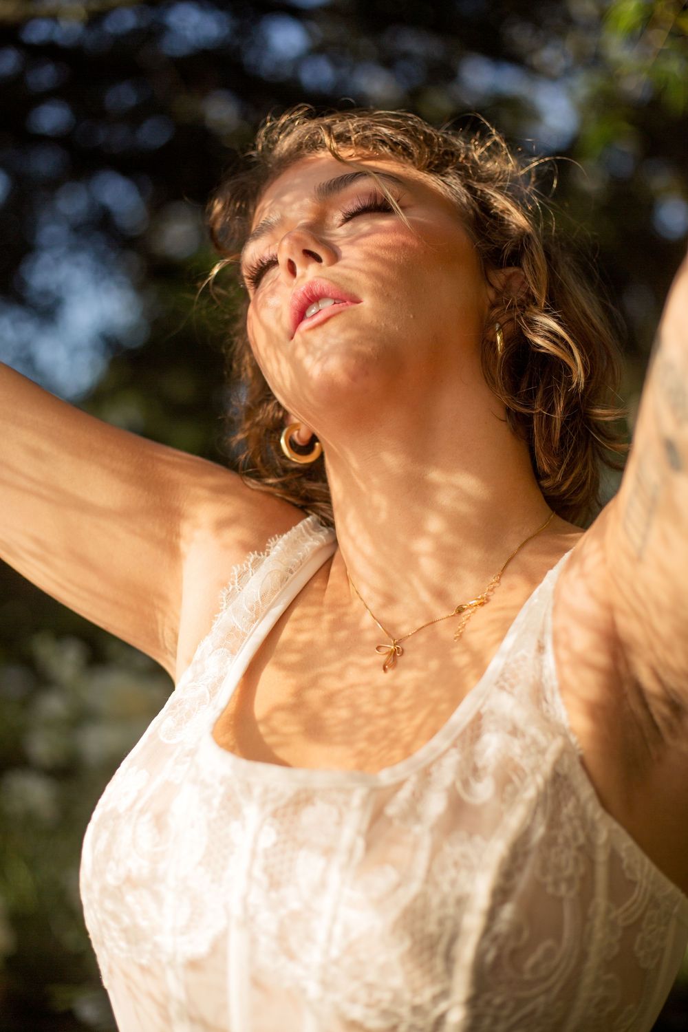 Person in white lace dress basking in warm sunlight with arms outstretched and eyes closed in peaceful moment.