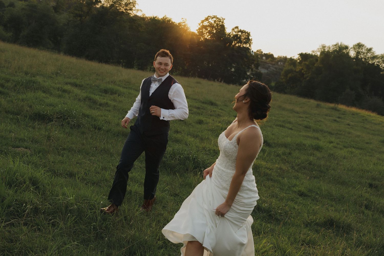 A couple shares a romantic moment at sunset in a grassy field while wearing wedding attire.