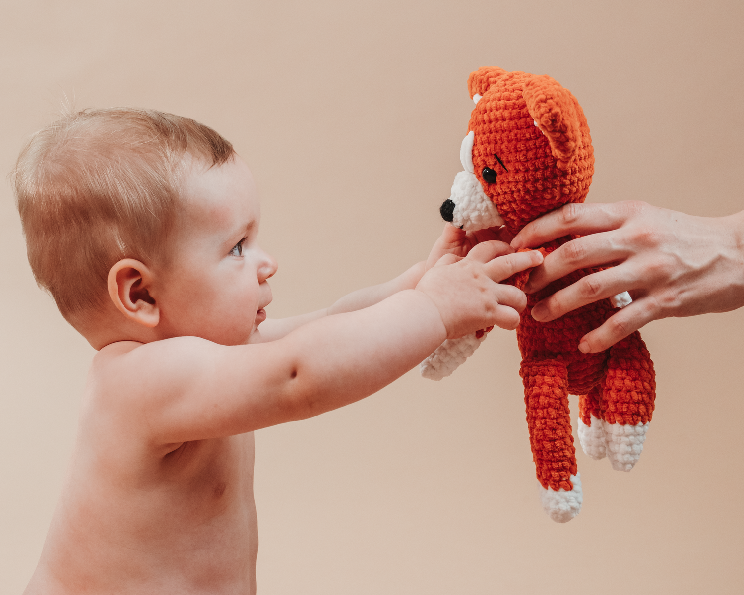 Baby reaching out to touch orange crochet stuffed animal toy.