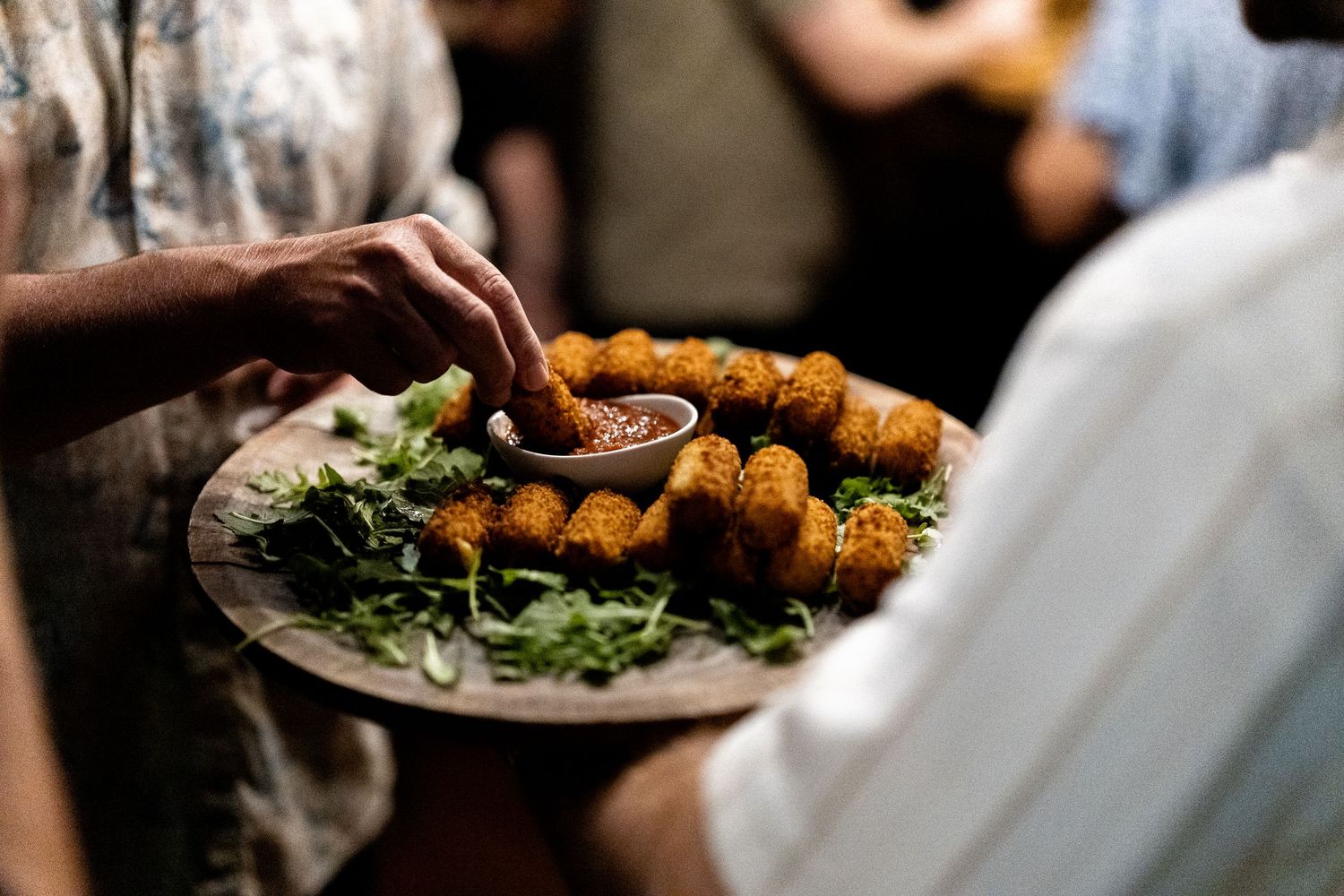 A plate of golden fried appetizers served alongside fresh green salad leaves being presented in soft focus.