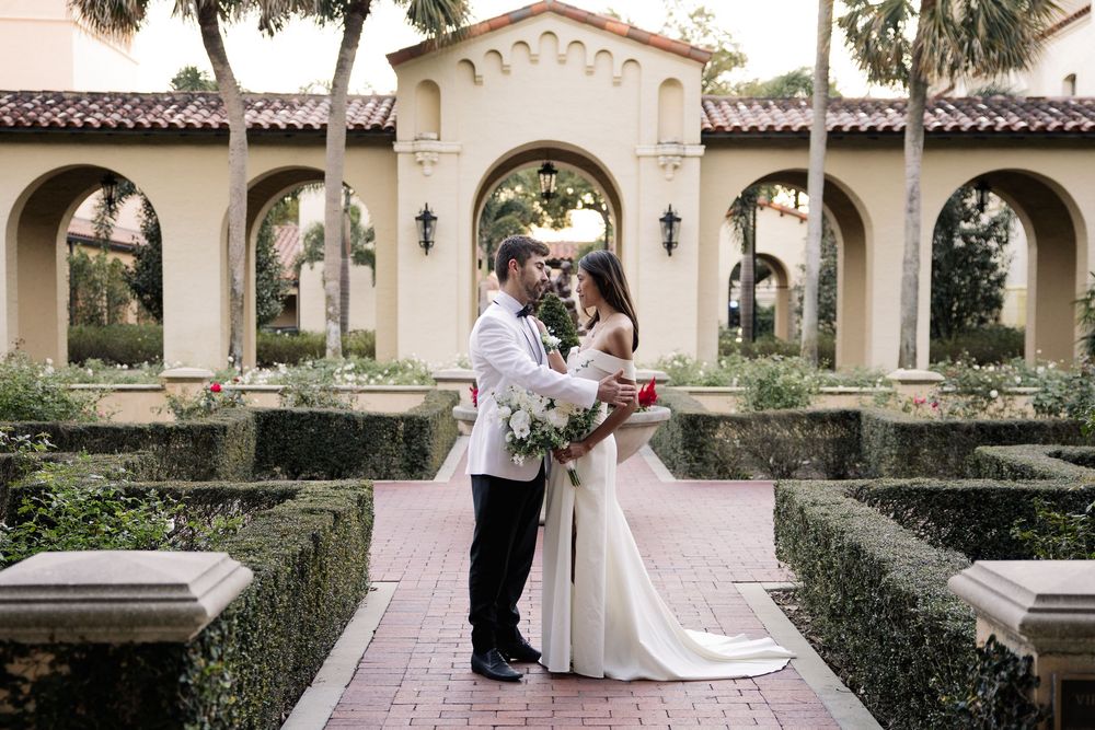 A couple embraces in an elegant Mediterranean courtyard with arched walkways and manicured gardens.