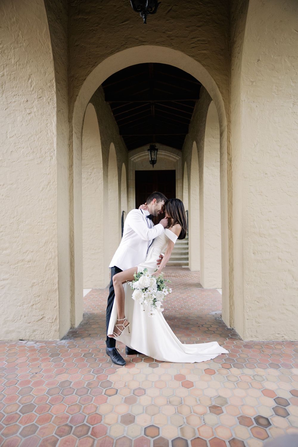A romantic wedding moment captured under an arched colonnade walkway with hexagonal brick pavers and cream colored walls.