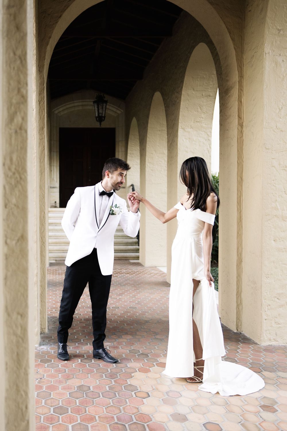 A couple in formal wedding attire sharing a romantic moment under elegant stone archways with terracotta flooring.