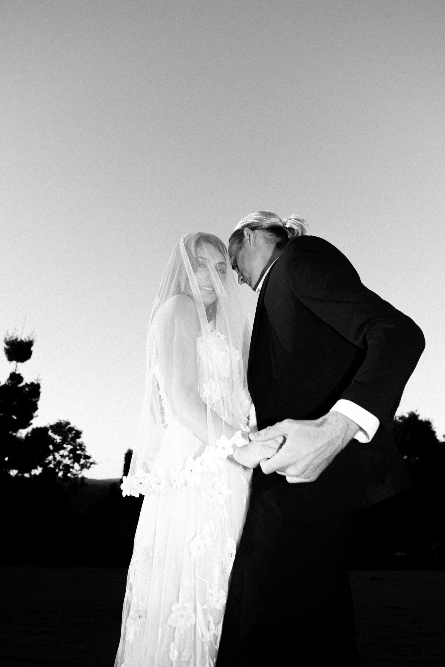 Black and white photo of bride and groom sharing a tender moment outdoors at dusk on their wedding day.