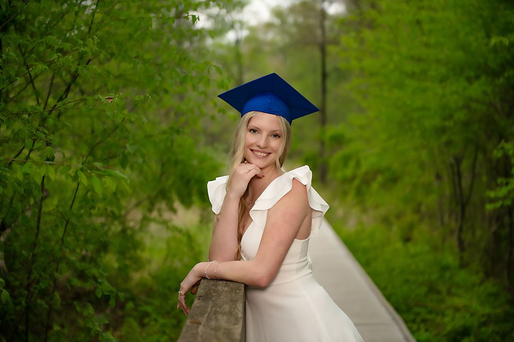 Graduation portrait on bridge with blue cap and white dress.