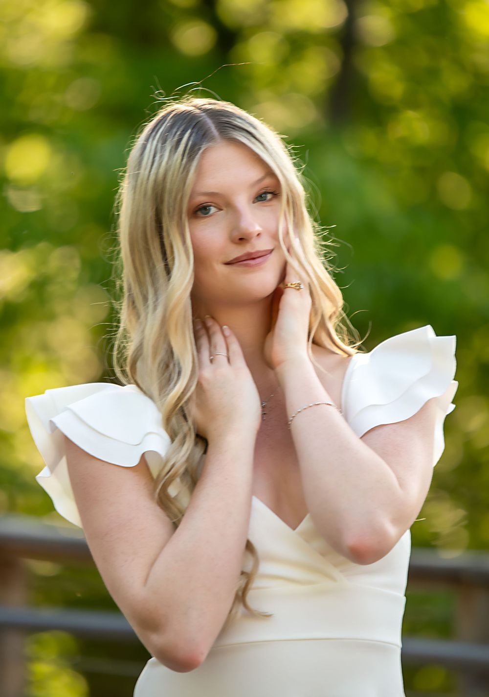 Elegant graduation portrait in a white dress against bokeh green background.