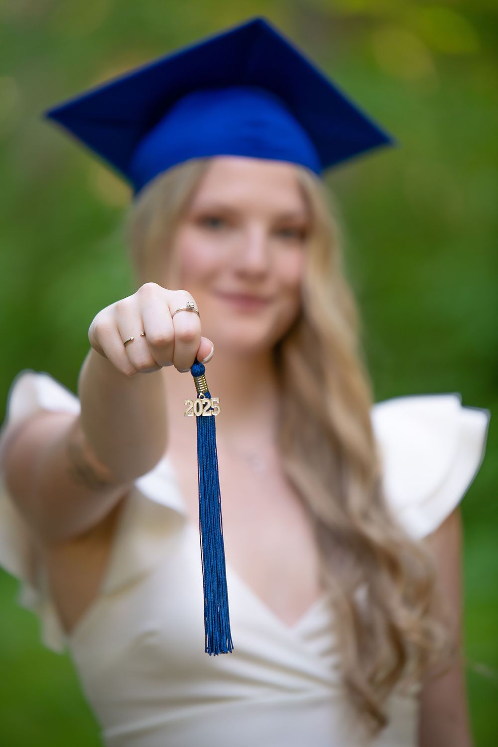 Graduate holds blue tassel while wearing cap and gown outdoors.