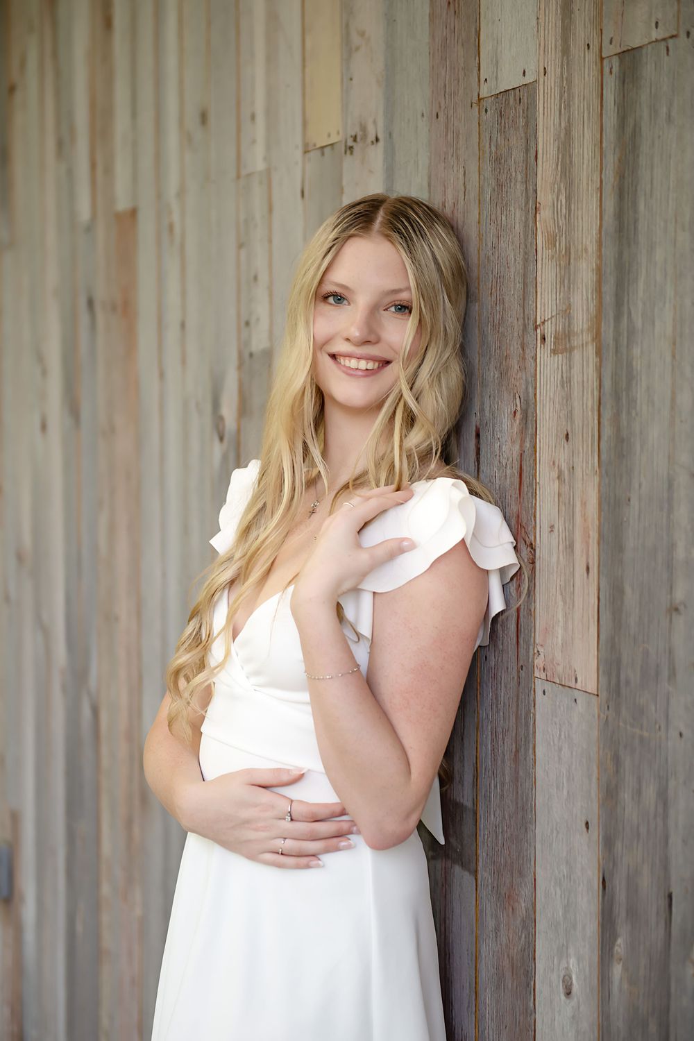 Senior portrait against rustic wooden wall wearing white dress with flutter sleeves.