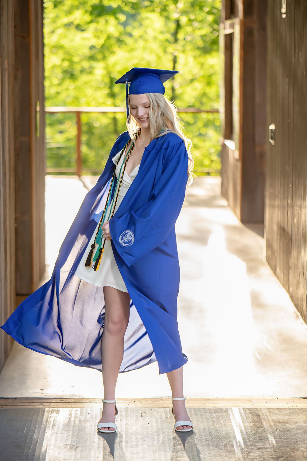 Graduate in blue cap and gown poses elegantly in covered walkway.