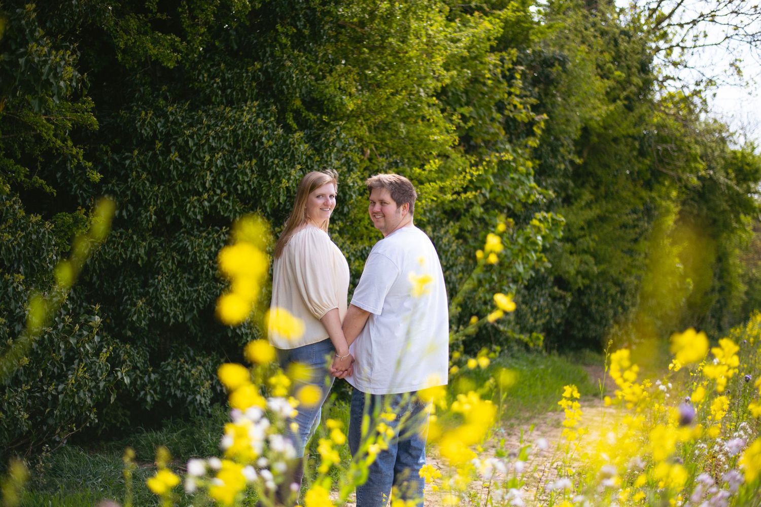 Couple sharing a romantic moment in a garden with yellow wildflowers in the foreground during golden hour.