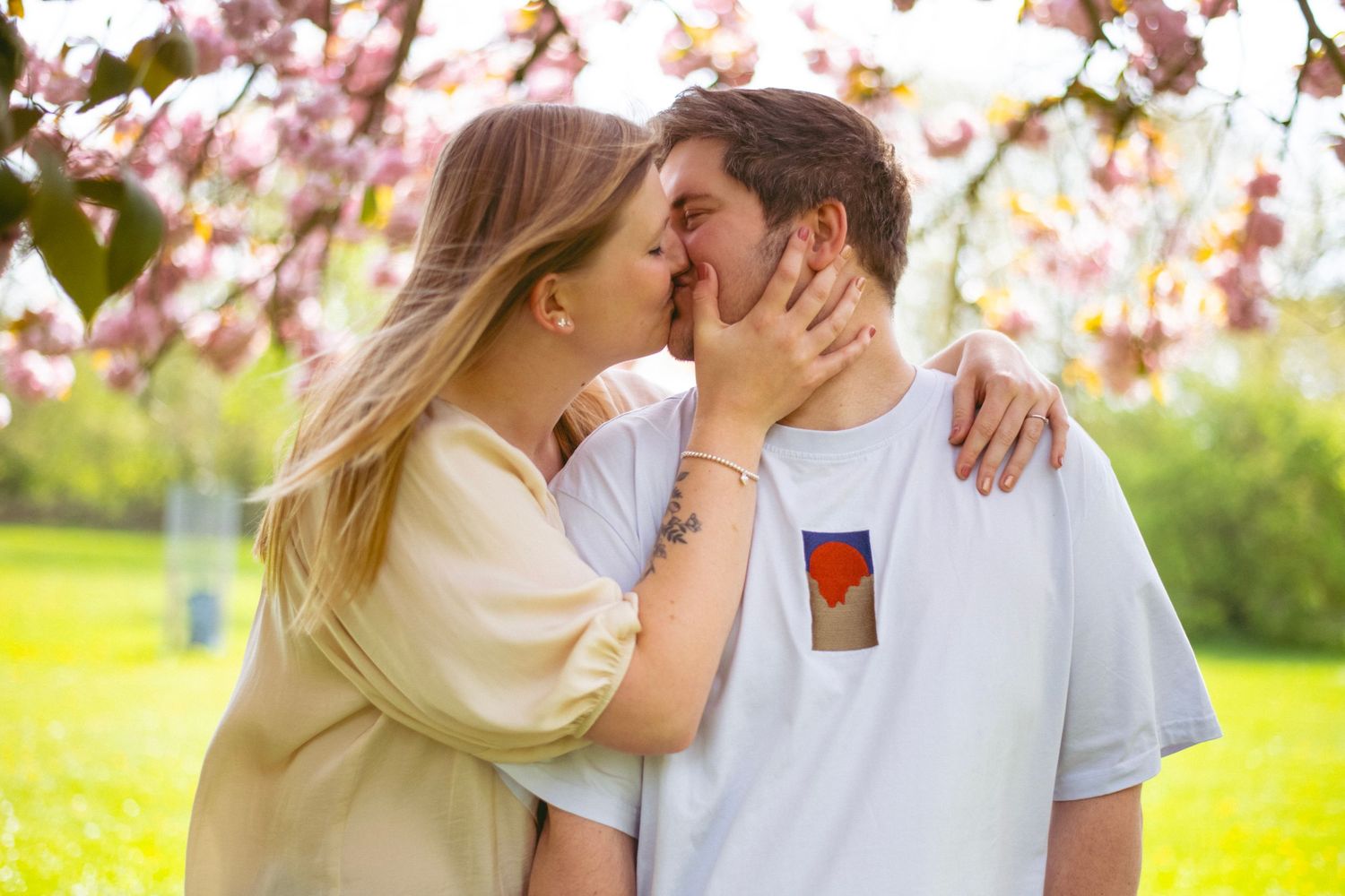 A romantic couple sharing a tender kiss in front of blooming cherry blossoms on a spring day.
