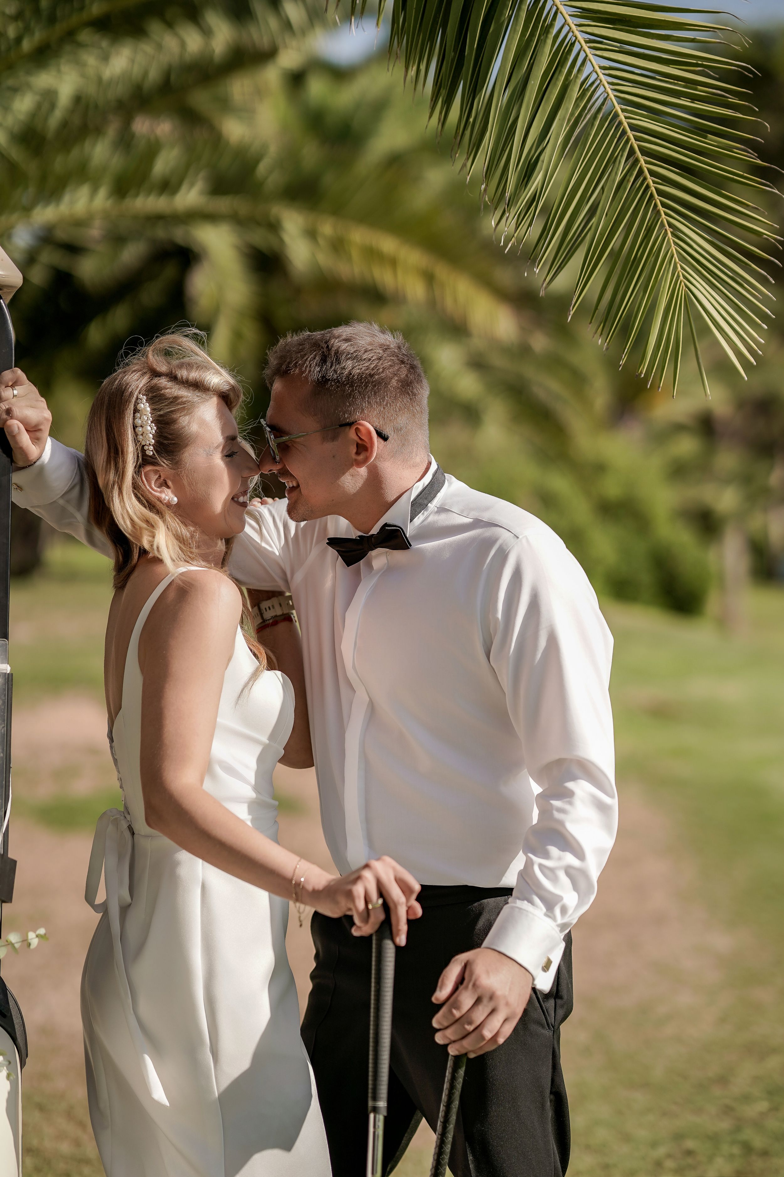 A couple in formal attire shares intimate moments outdoors under palm trees in a romantic photoshoot sequence.