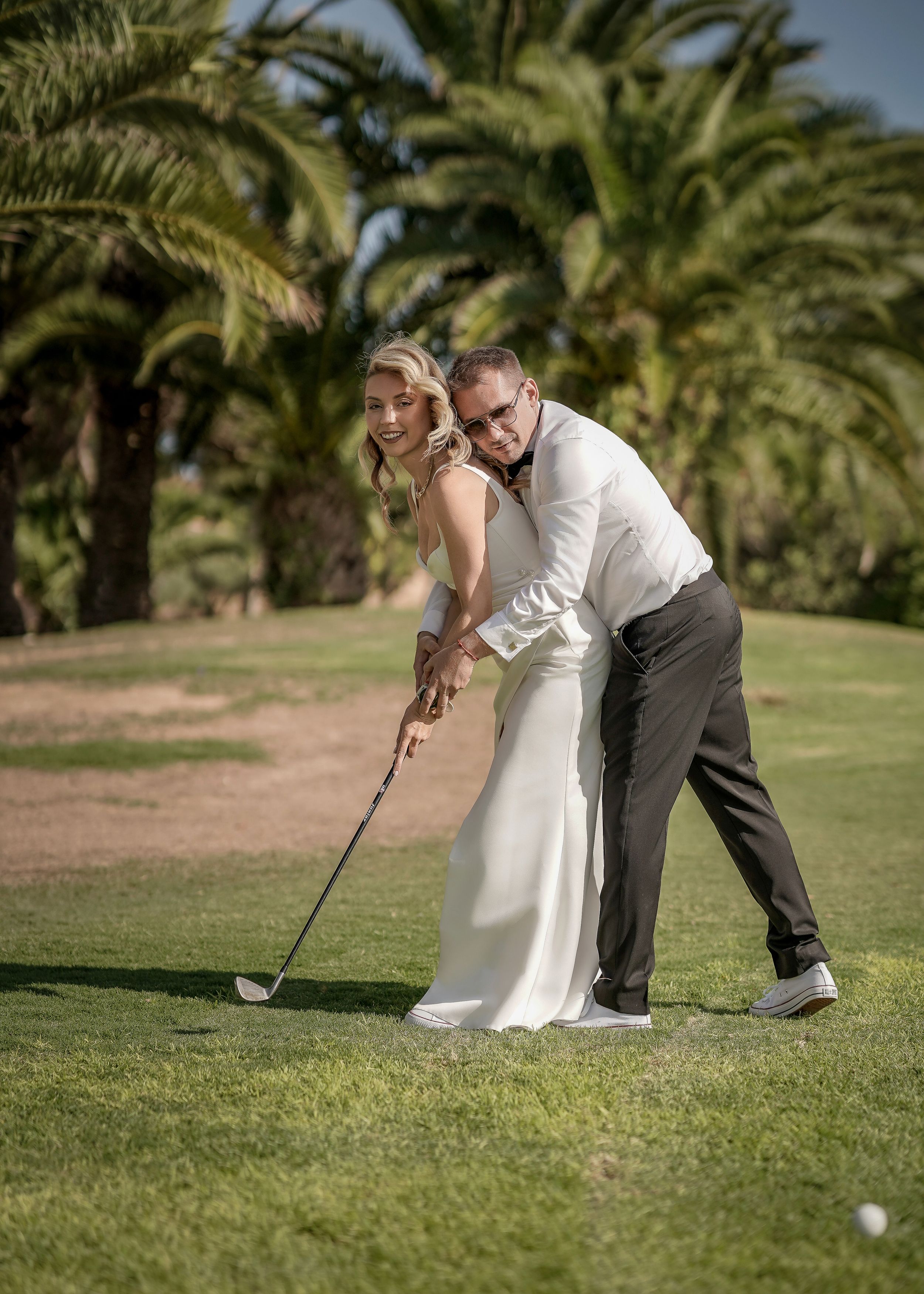 Couple plays golf together on a tropical course with palm trees in the background during a wedding photoshoot.