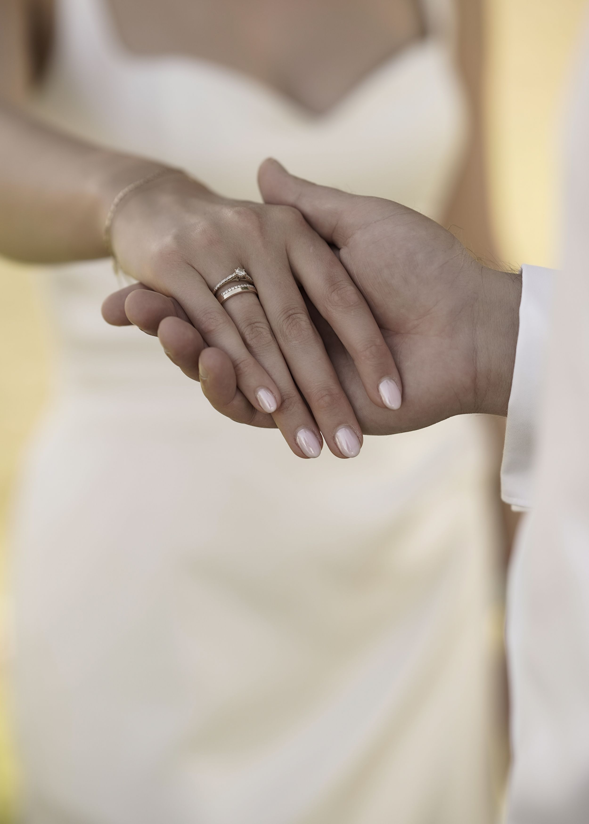 Close-up view of hands wearing wedding rings against a soft white background.