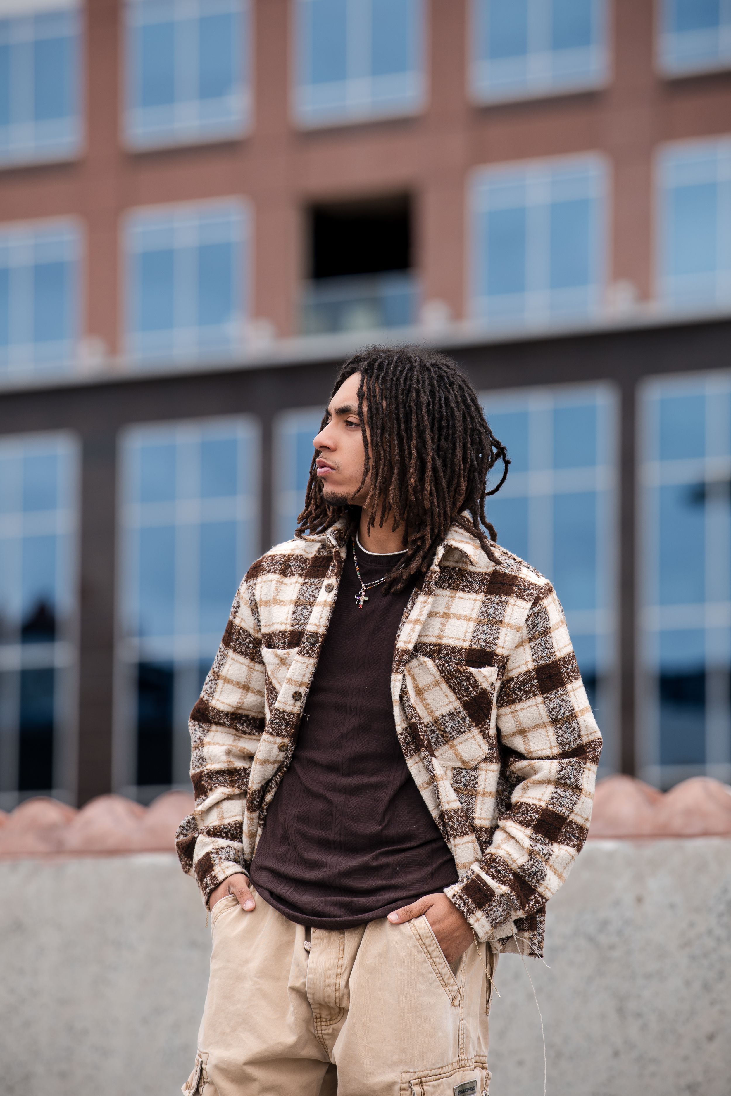 Casual street style featuring plaid jacket and khaki pants against modern building facade.
