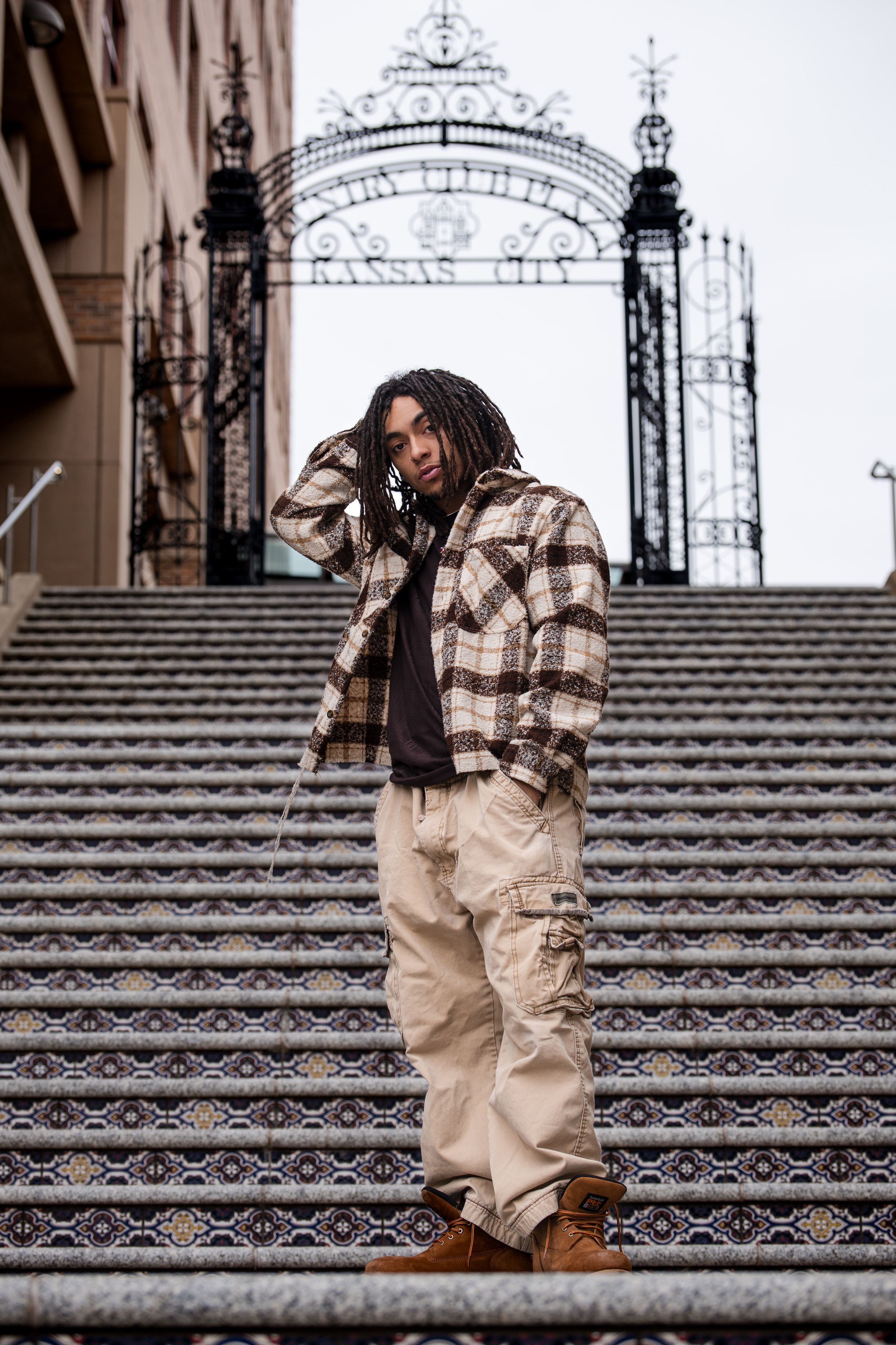 Urban fashion portrait on ornate stone steps with decorative iron archway.