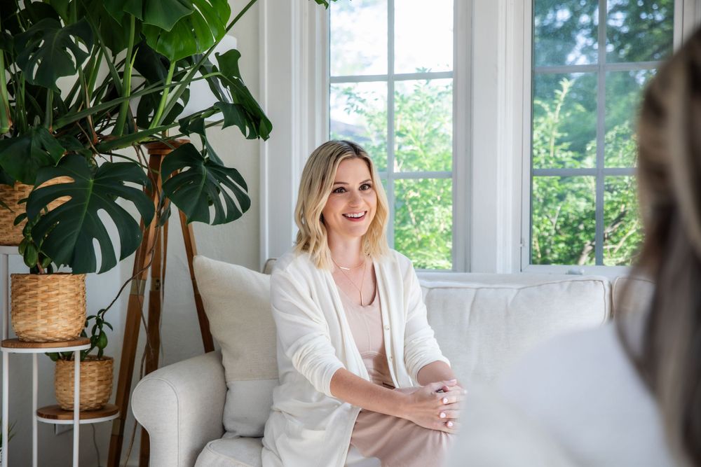 Person in white cardigan relaxing on couch in bright room with large indoor plants.