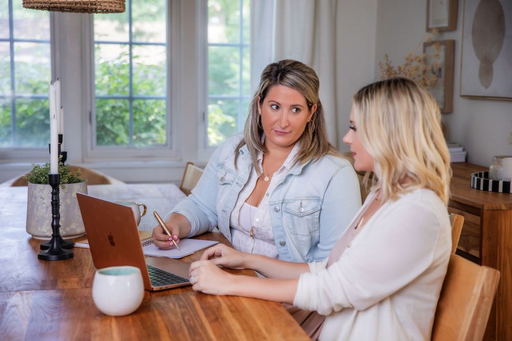 Two people having a business meeting at wooden table with laptop and drinks.