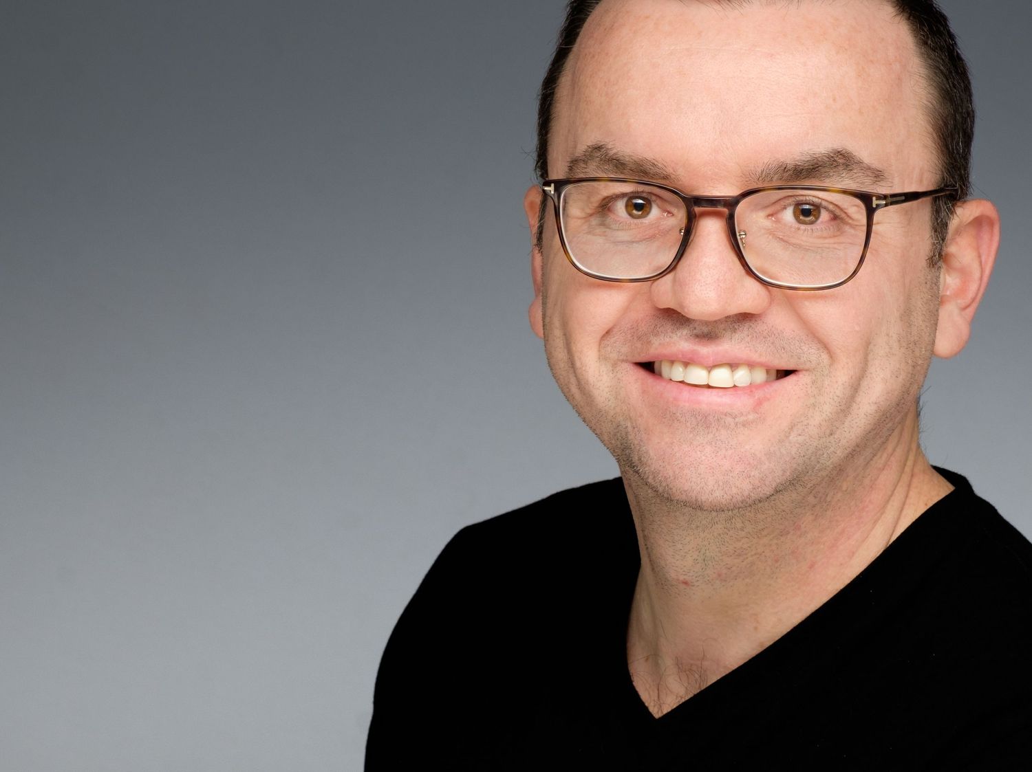 Professional headshot of someone in a navy blazer and white dress shirt smiling with arms crossed.