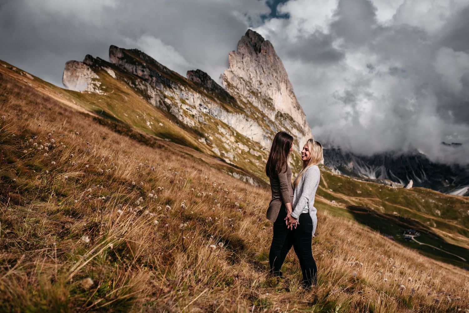 Lesbian couple holding hands in front of the mountains of Seceda, in Italy.