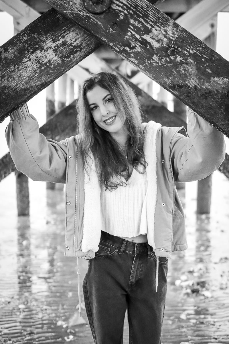 Monochrome image of a female standing underneath a boardwalk in the winter for senior portraits.