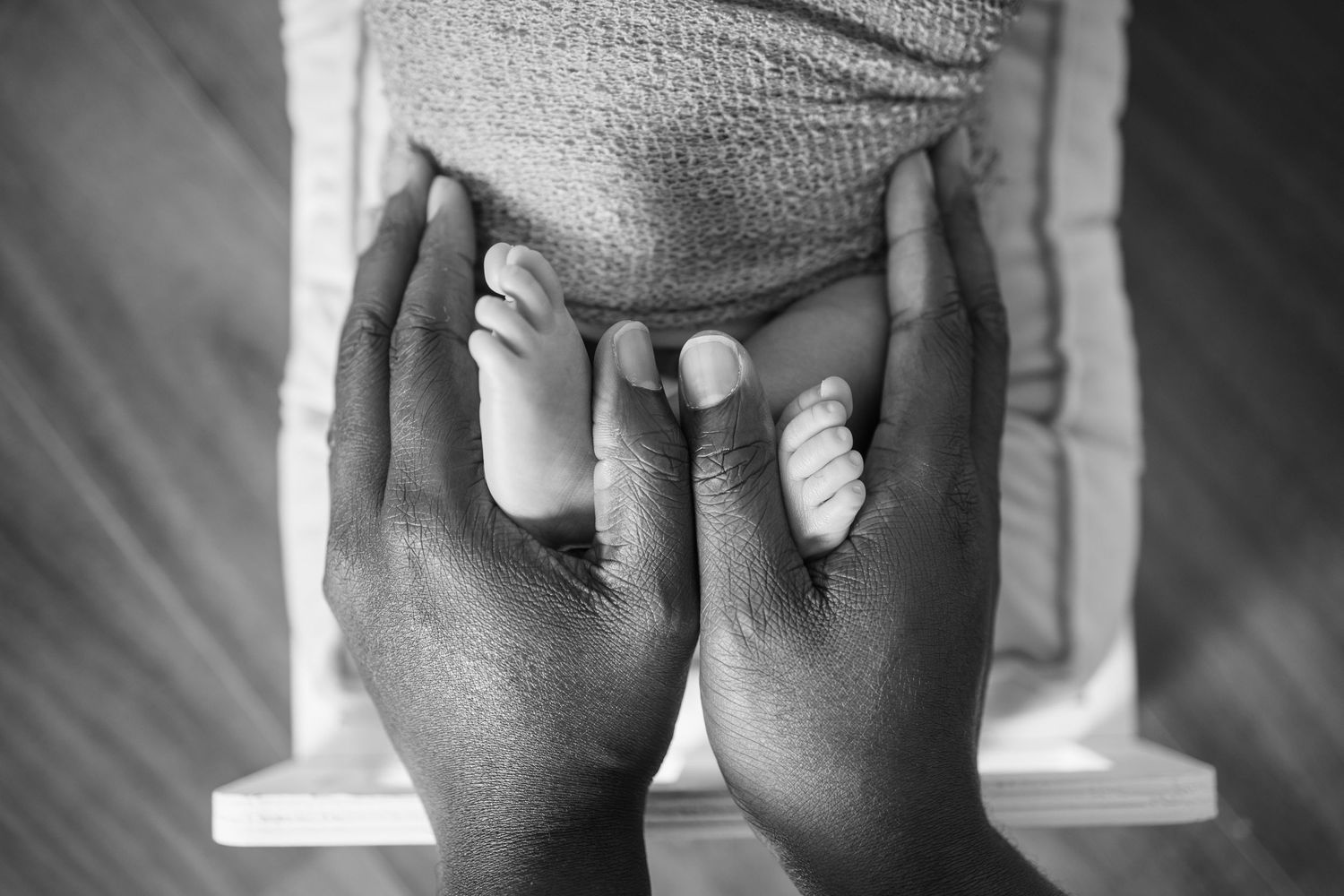 Black and white close-up photograph of tiny baby feet resting on an adult's hands and lap. Newborn and maternity photographer in Richmond VA