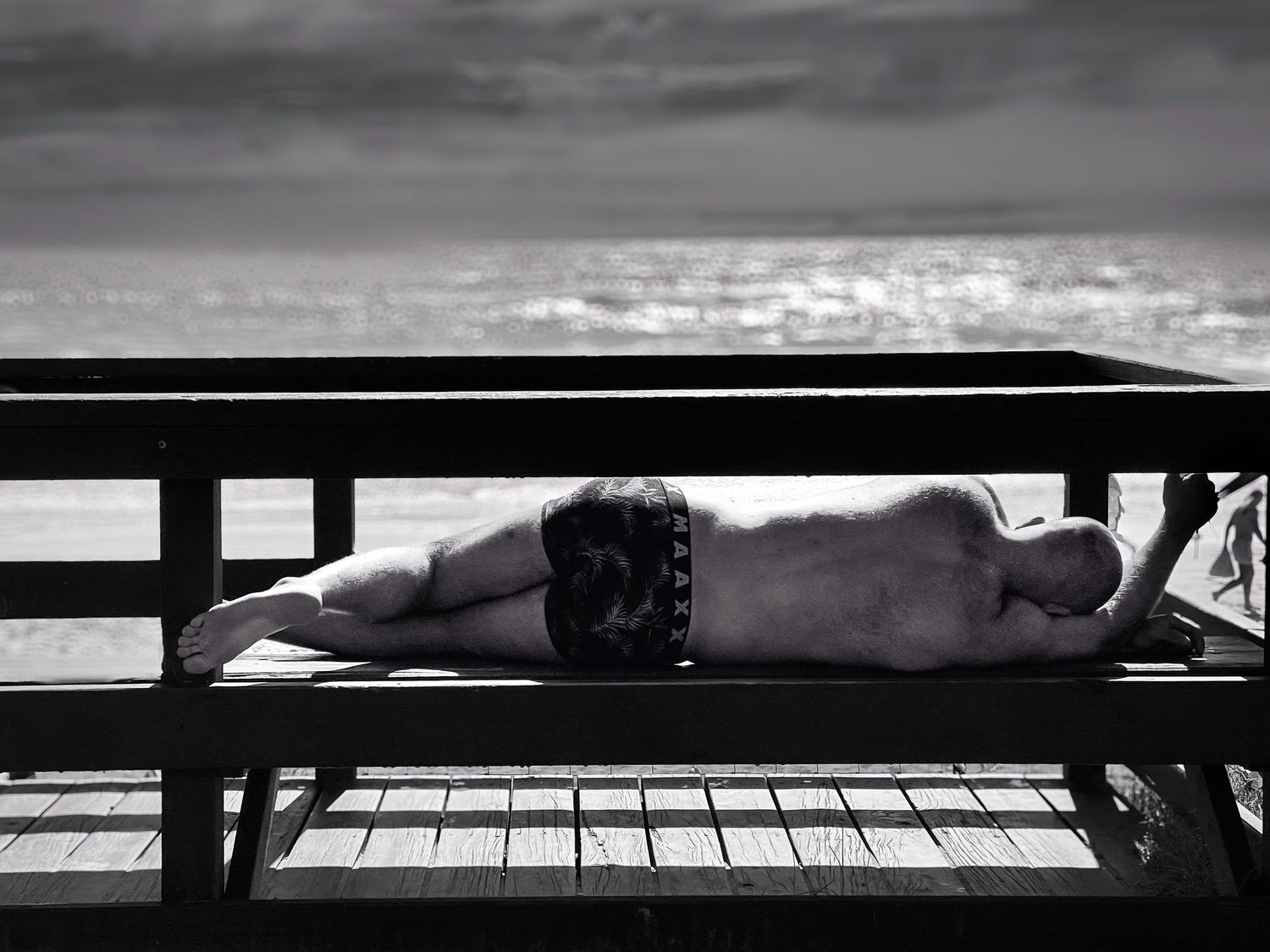 Photograph of a man sleeping on a beach at the beach.