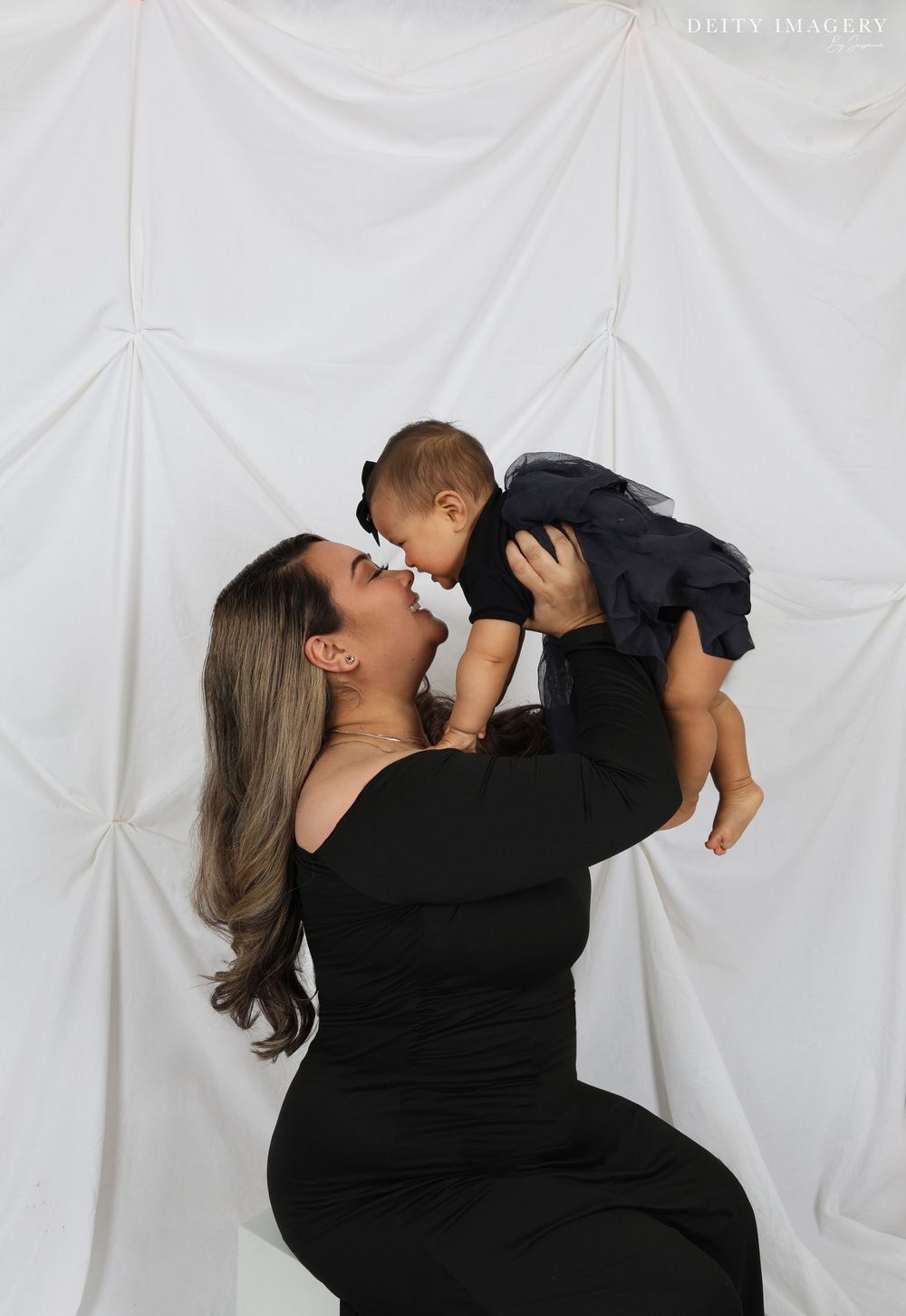 A tender moment captured in black and white showing a parent lifting and embracing a small child against a white backdrop.