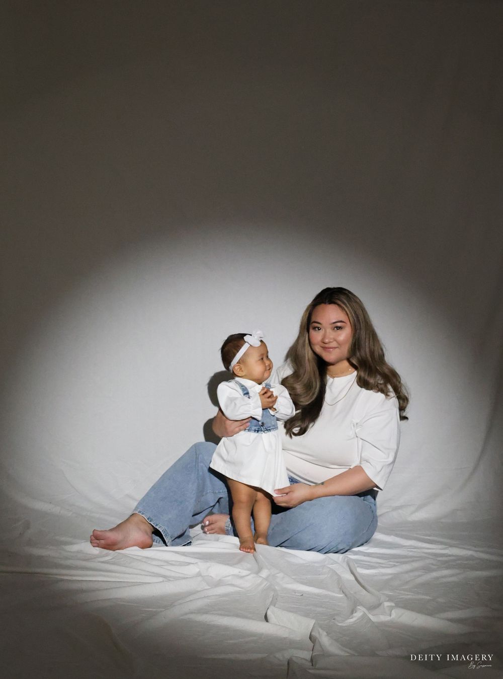 A series of intimate maternity portraits showing a couple resting together on white bedding in soft, moody lighting.