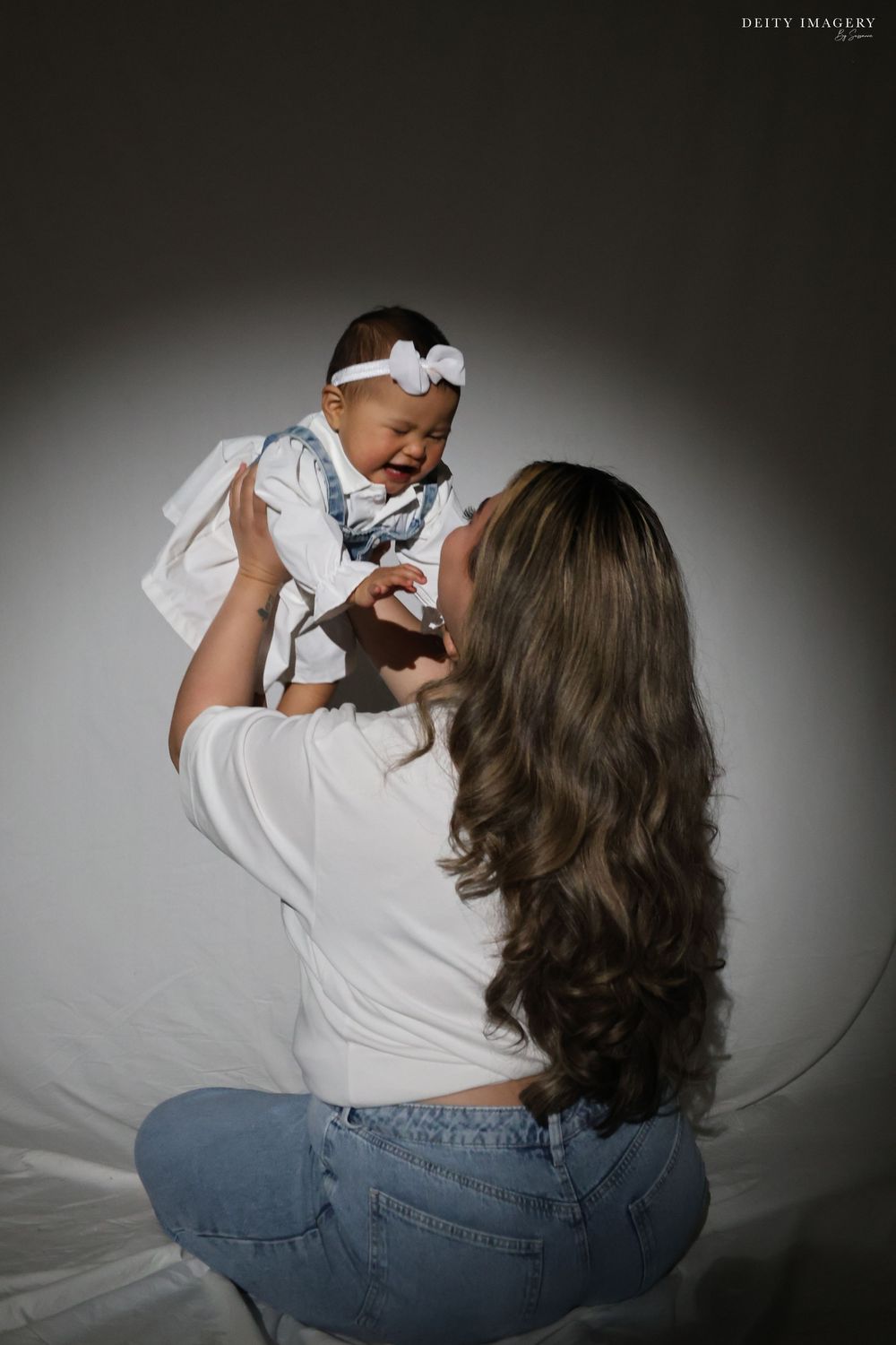 A tender moment between parent and baby in white against a dark background during a studio photoshoot.