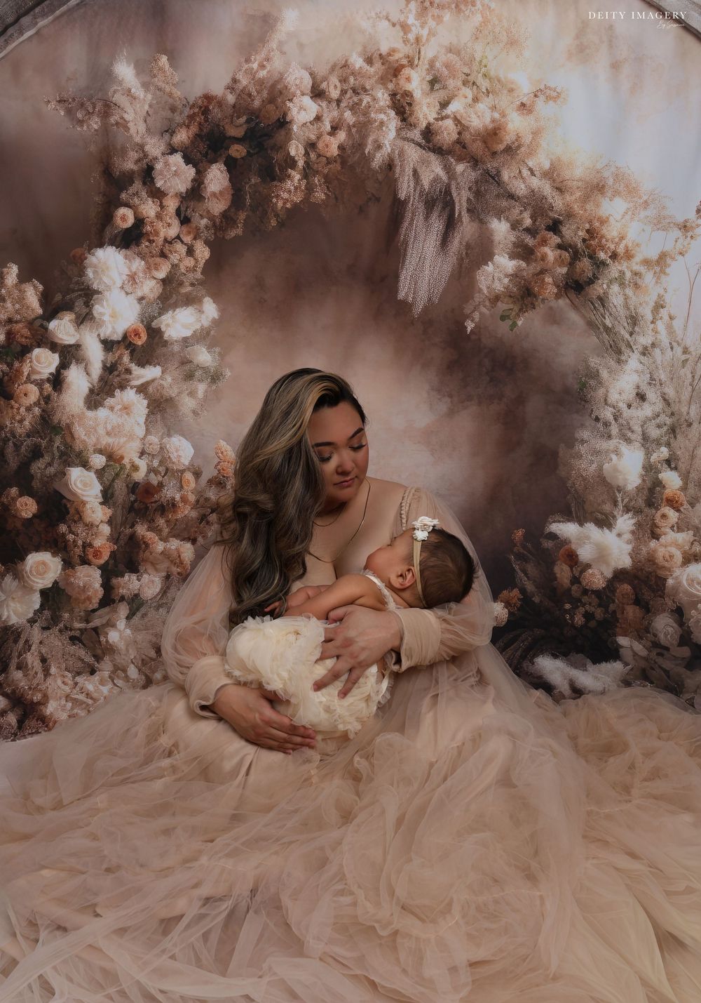 Dreamy maternity portrait surrounded by soft white floral arrangements in ethereal sepia tones.
