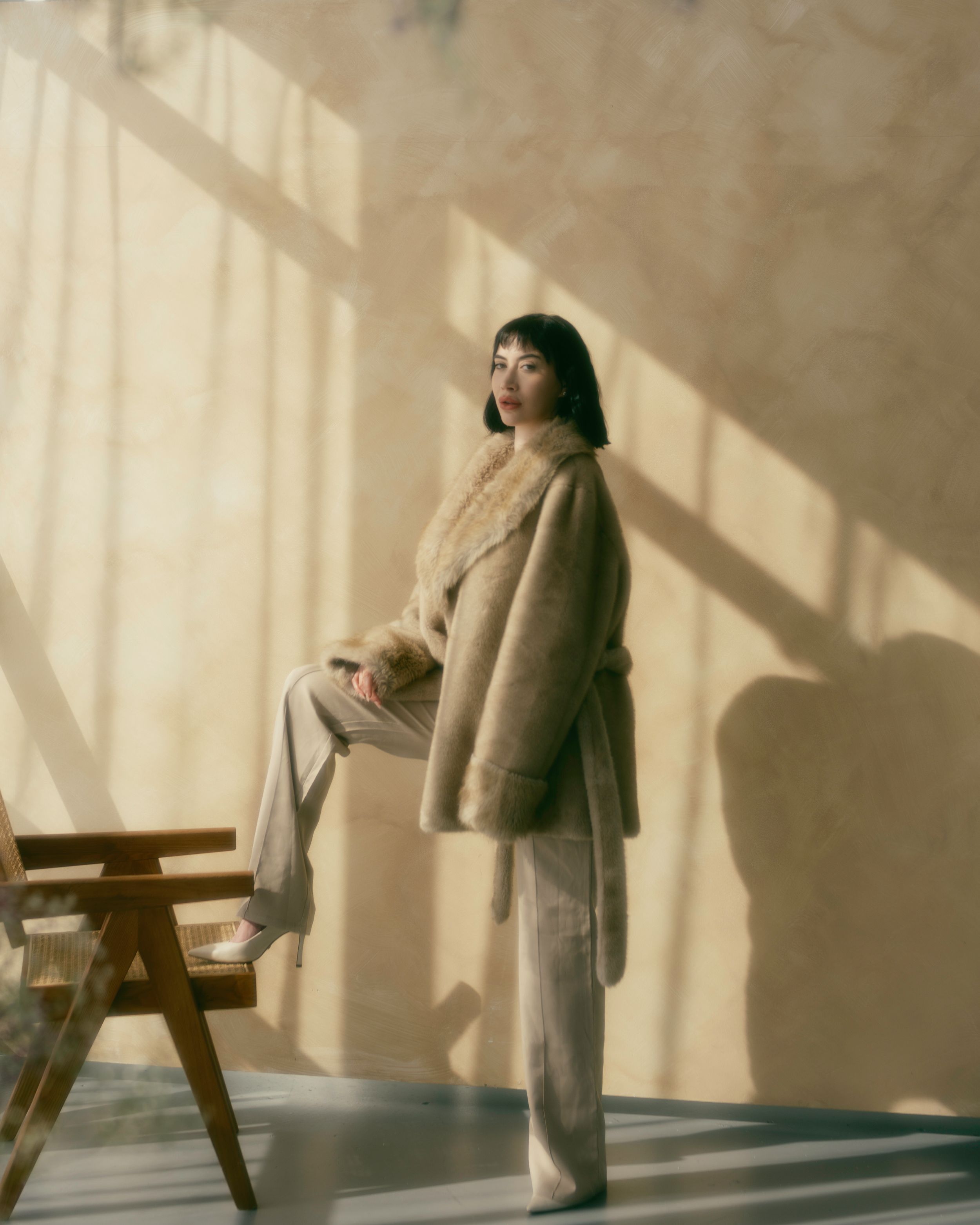 Vintage-inspired portrait with natural window light casting dramatic shadows on a beige wall.